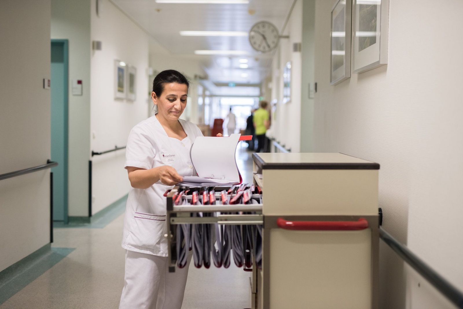 Krankenschwester sichtet medizinisch-pflegerische Dokumentationsunterlagen und steht am geöffneten Visitenwagen